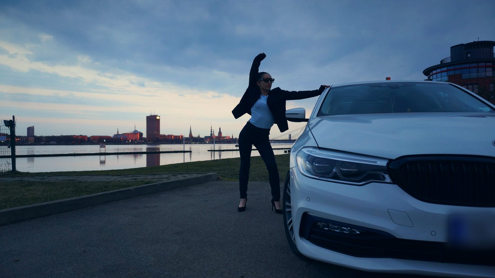 Девушка в динамичной позе у белого BMW на набережной