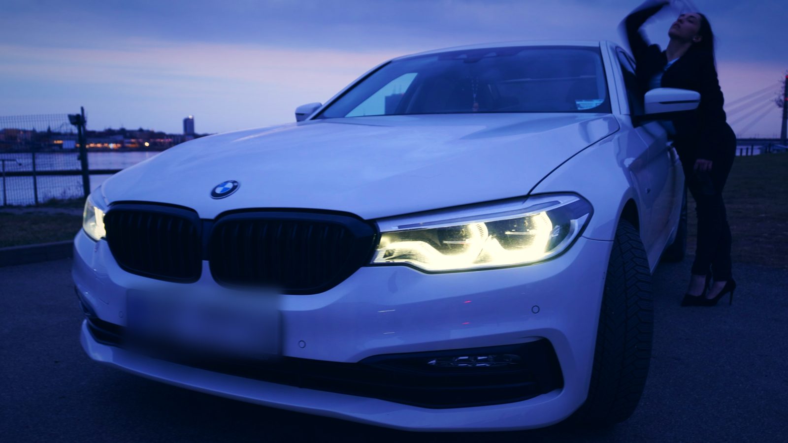 Белый BMW с включёнными фарами в синих сумерках