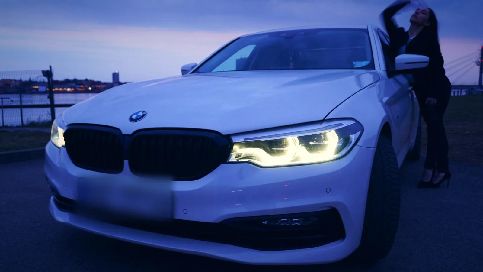 Weißer BMW mit eingeschalteten Scheinwerfern in der blauen Stunde