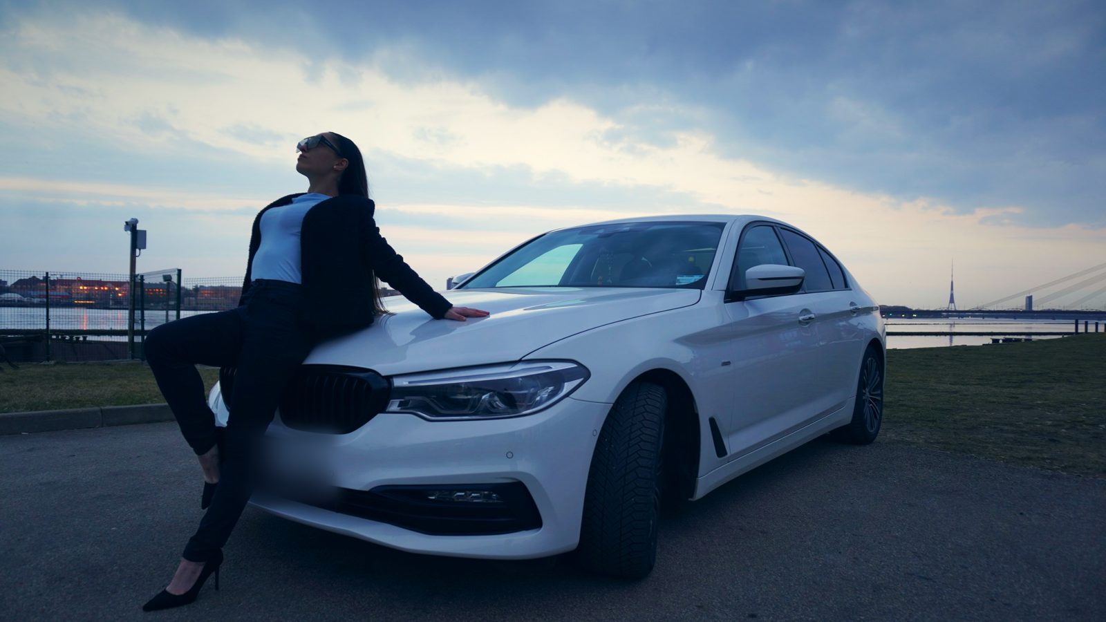 Девушка сидит на капоте BMW и смотрит в небо