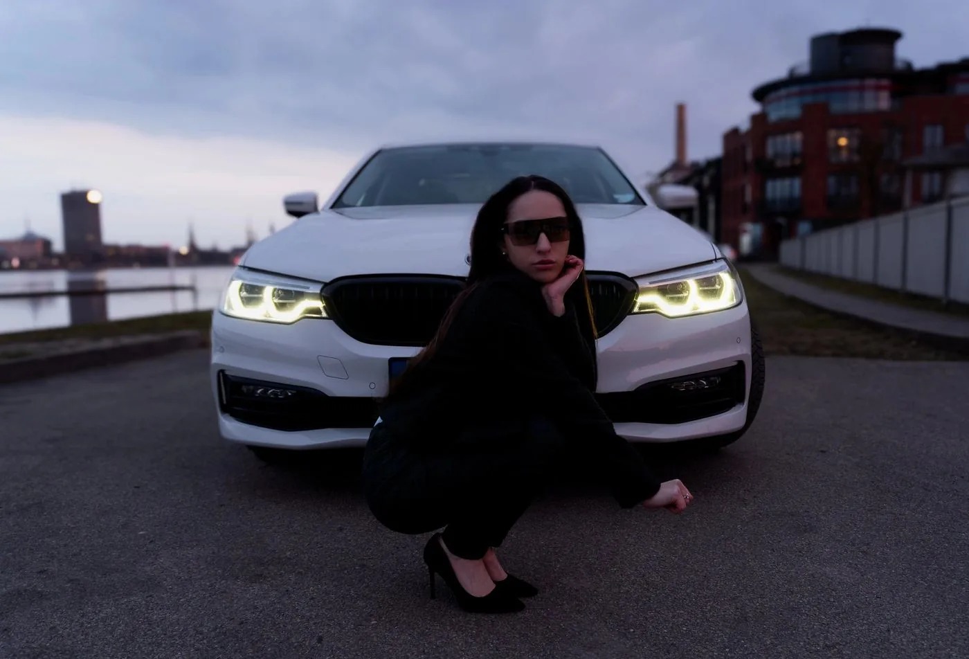 Frau neben einem weißen BMW mit eingeschalteten Scheinwerfern