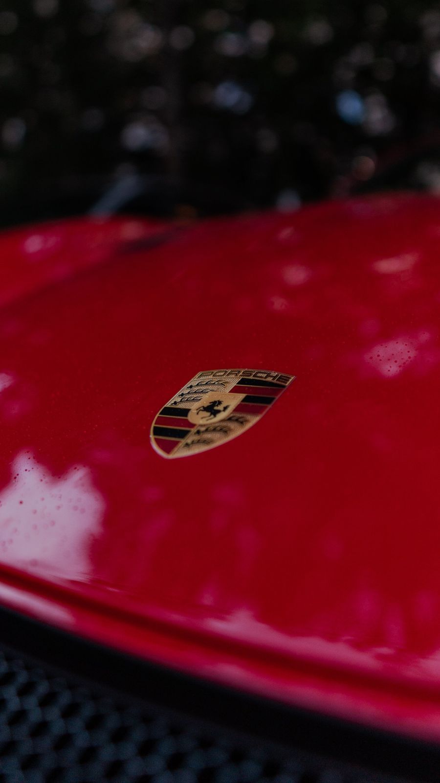 Эмблема Porsche на красном капоте с каплями
